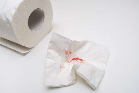 Used sheet of bloody toilet paper and a roll on white background, hemorrhoids and rectal bleeding concept.の写真素材
