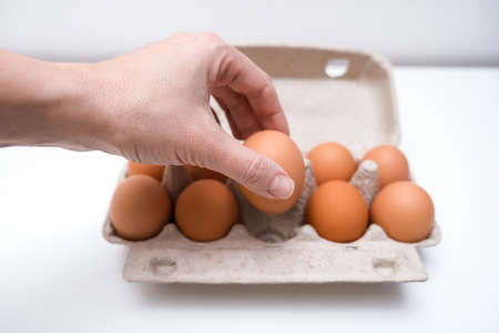 Hand taking one brown chicken egg from a carton box, container for breakfast.の写真素材