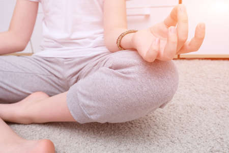Unrecognizable meditating teenage boy sitting on a carpet at home, spiritual yoga buddhism practics, relaxation and tranquility conceptの写真素材