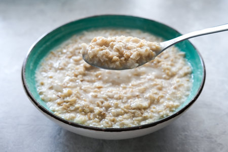 A spoon of cooked oats porridge above a green bowl, healthy breakfast and dieting product close up, tasty vegan foodの写真素材
