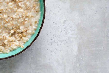 A green bowl of cooked oats porridge close up, healthy breakfast and dieting product on grey backgroubd with copy spaceの写真素材