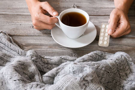 Woman hands holding a cup of hot tea and a blister of pills, seasonal winter infections, flu treatment conceptの写真素材