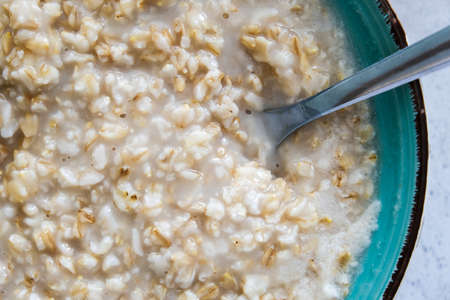 A green bowl of cooked oats porridge with a spoon close up, healthy breakfast and dieting product close upの写真素材