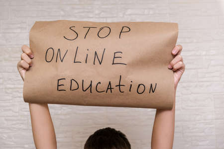 A childs hands holding a banner with a sign stop online education, struggle against distance...