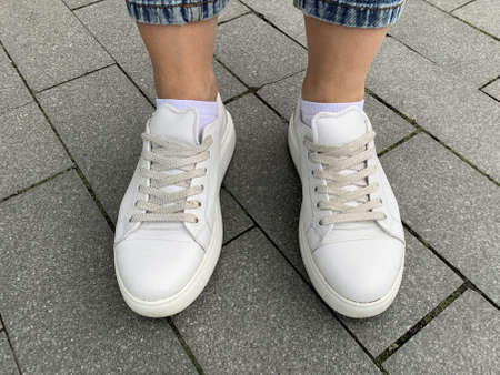 Woman legs wearing white leather laced sneakers outdoors, trendy shoes for urban life, walking in...