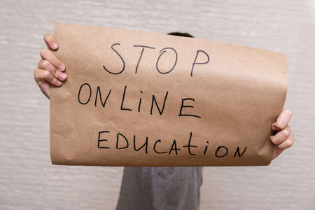 A childs hands holding a banner with a sign stop online education, struggle against distance learningの写真素材