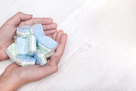 Hands holding many green and blue dishwasher soap tablets in water-soluble packaging, copy space