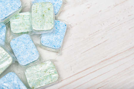 Green and blue dishwasher soap tablets in water-soluble packaging close up on the table with copy spaceの写真素材