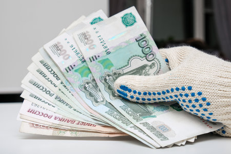 Hands of a worker, handyman, builder in protective gloves holding money, salary, payment for work in russian roublesの写真素材