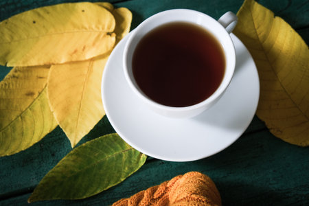Top view of white ceramic cup of tea on green background with yellow autumn fall leavesの写真素材