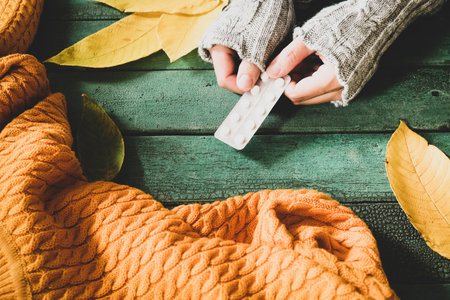 Woman hands wearing cozy warm knitted sweater holding a blister of pills as autumn flu treatmentの写真素材