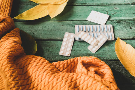 Many blister of pills on background with yellow fall leaves and warm sweater, seasonal flu conceptの写真素材