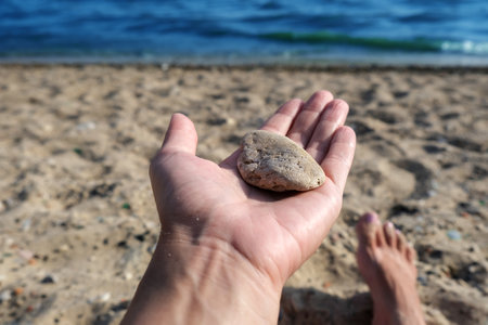 A stone lying in a womans hand on the sea, hot sand, relax, zen, serenityの写真素材
