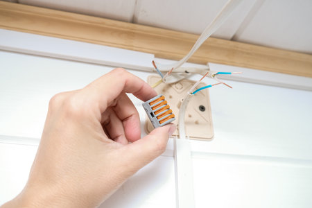 Electrician holding an electric clamp to connect wires on the wall, bare wires on backgroundの写真素材