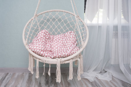 White wicker swing hanging chair with pink pillow, cute light modern interior bedroom, cozy houseの写真素材
