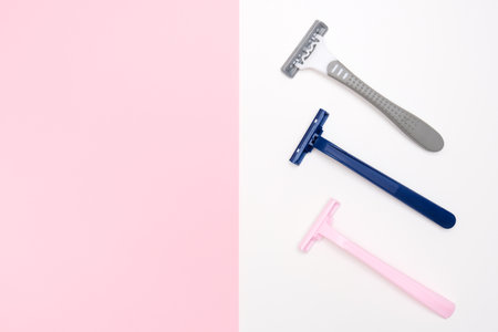 Three disposable razor blades of different colors for removing, shaving unwanted hair on face and body on white and pink background with copy spaceの写真素材
