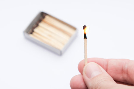 Hand holding burning match stick on white backgroundの写真素材