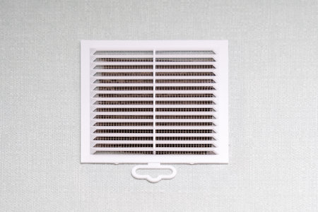 A white air vent is situated and hanging on a pristine white wall, creating a subtle yet functional element in the rooms designの写真素材