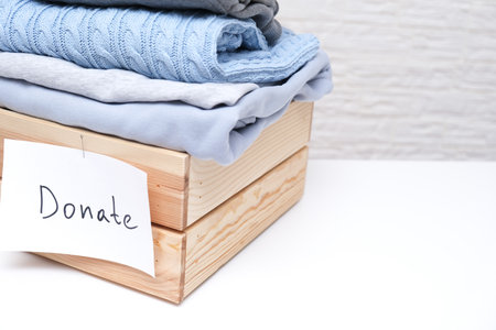 Inside a rectangular wooden box, there are various clothes neatly arranged along with a note that kindly requests to donate themの写真素材
