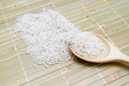 A beautifully crafted wooden spoon is filled with fluffy white rice and is thoughtfully positioned on a textured bamboo matの写真素材