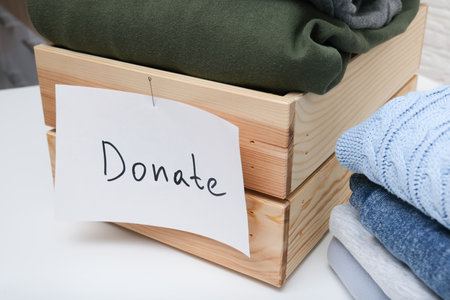 Inside a rectangular wooden box, there are various clothes neatly arranged along with a note that kindly requests to donate themの写真素材