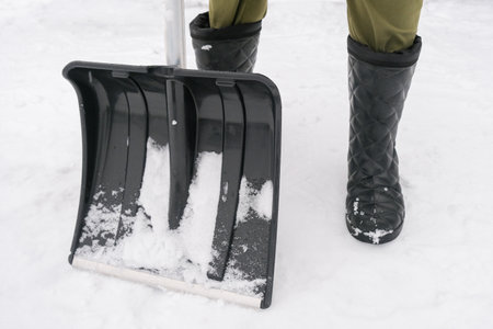 An unrecognizable person in snow boots holding a plastic shovel in order to clean, remove snow from...