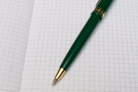 A blank notebook with a green pen lying on top. The notebook is open and ready for writing.の写真素材