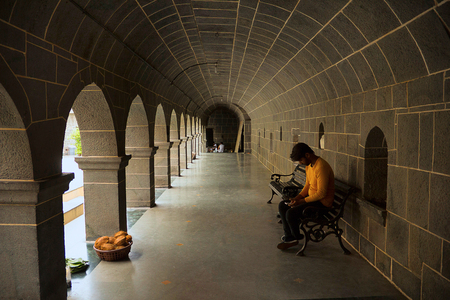 Young Indian man dressed in orange checking his mobile sitting at the porch of Vitthal Mandir templeのeditorial素材