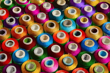 Close view of sewing threads of various color on spindles 