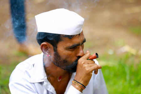 Man in white cap wearing a white shirt smoking, side profile. Pandharpur festivalのeditorial素材