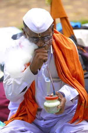 Man in white cap wearing a white shirt smoking, side profile. Pandharpur festival