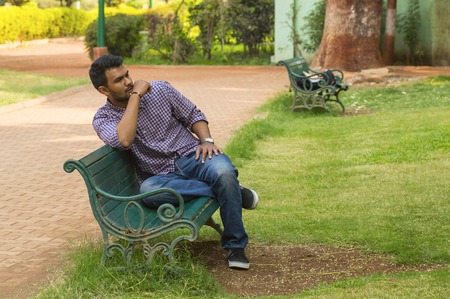 Young guy looking away sitting on a bench in a parkの写真素材