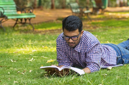 Handsome young boy reading while lying on grass in parkの写真素材