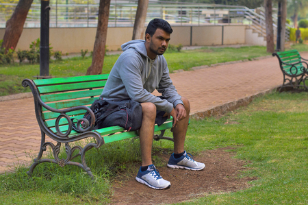 Young and handsome sportsman sitting on a wooden bench in a park