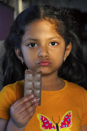 Small girl eating chocalate bar with a serious or guilty expression with sunlight on her face