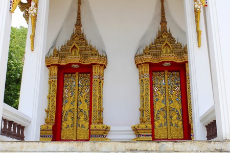 Doors and windows of the temple adorned by intricate wooden carvings in golden color depicting Buddha's life familiarized by Jataka Tales, at Ban Bung Sam Phan Nok, Phetchabun, Thailandの写真素材
