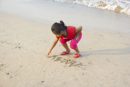 Little girl writing on wet sand at Alibag beach, Konkan, Indiaの写真素材