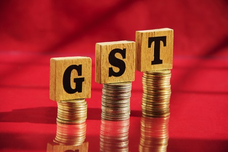 Wooden letters GST and money coin stack on red table background, financial conceptの写真素材