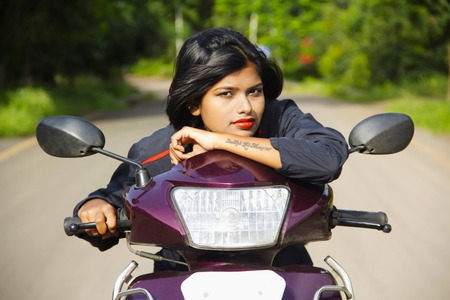 Close-up of young Indian girl resting on two wheeler scooter handle and posing for camera, Pune