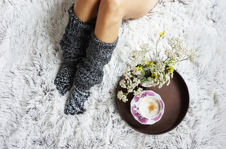 legs of girl in warm woolen socks and a cup of coffee warming, winter morning at home