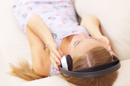 Young attractive girl lying on sofa, listening to music in headphonesの写真素材