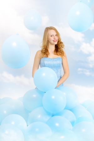 Beautiful girl in a blue dress with balloons  background of cloudsの写真素材