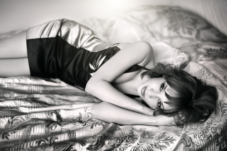 Young beautiful woman lying on a bed on dark backgroundの写真素材