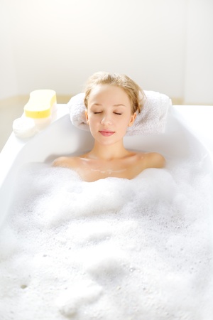 Attractive girl relaxing in bath on light backgroundの写真素材