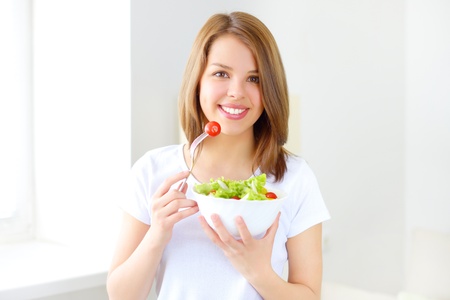 Teenager girl eating salad on light backgroundの写真素材