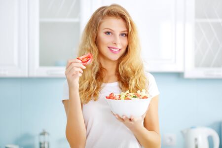 Beautiful young woman with fresh salad on a light backgroundの写真素材