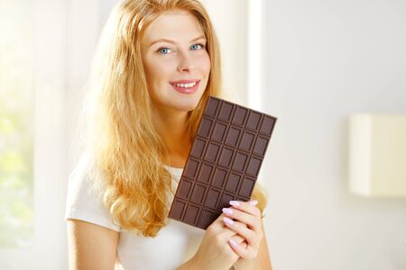 Young woman eating chocolate on a light backgroundの写真素材