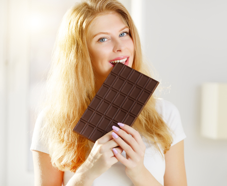 Young woman eating chocolate on a light backgroundの写真素材