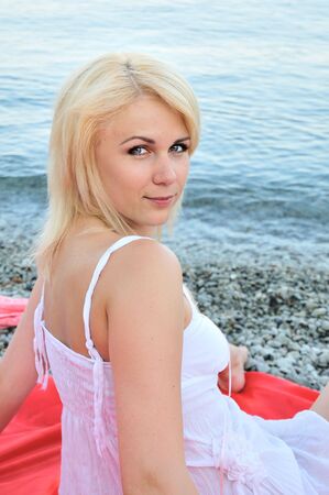A beautiful girl sitting near the sea water she is wearing white short dressの写真素材