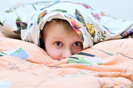 little boy laying under the pillow and watching something frightful on TVの写真素材